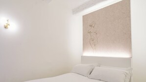 A bedroom with a bed, white bedding, and a wall-mounted light fixture.