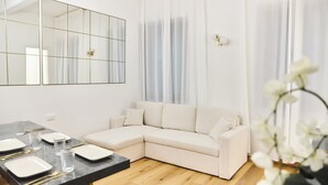 A modern living room with a sectional sofa, a dining table with plates and cutlery, and a large mirror on the wall.