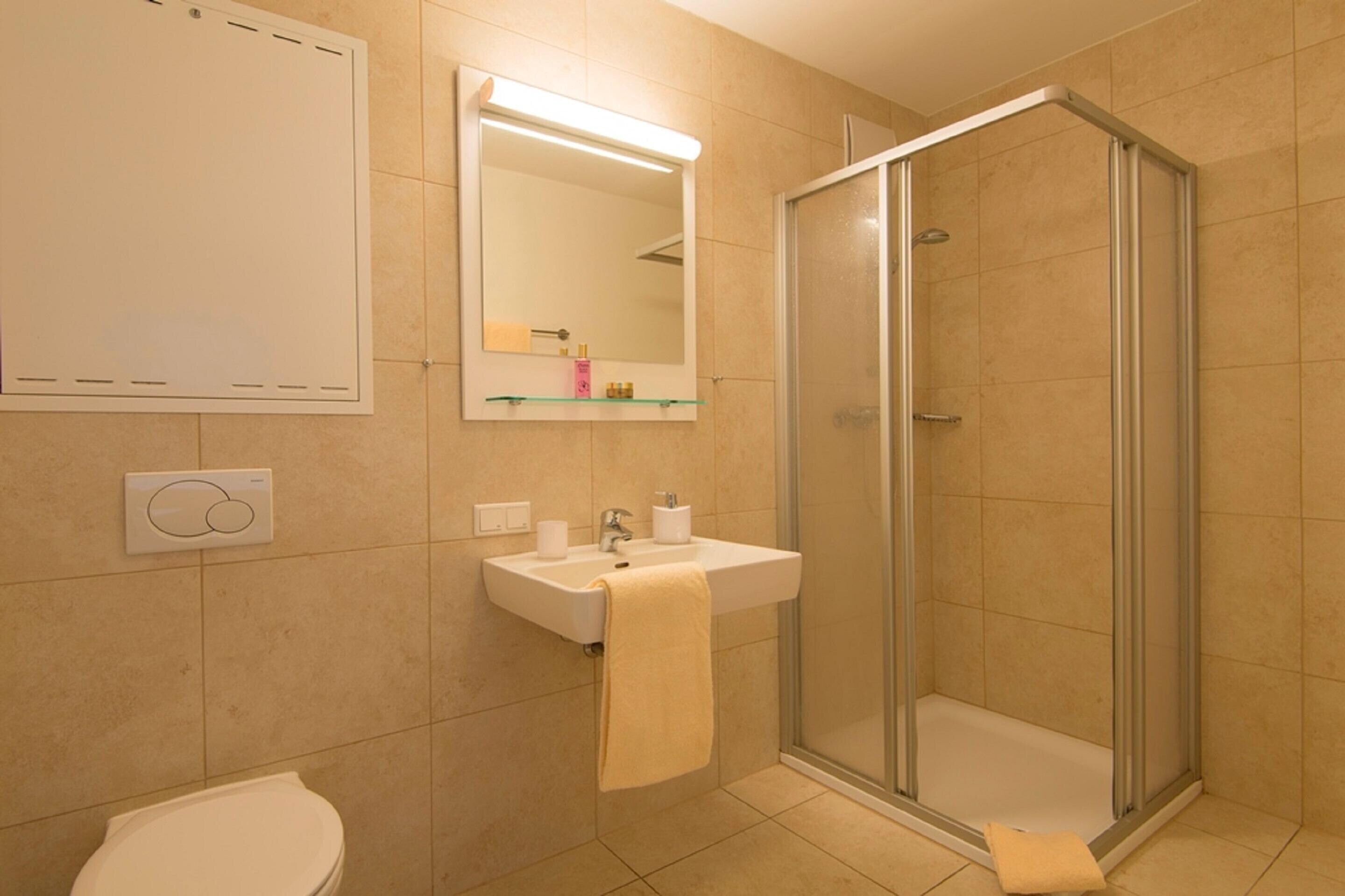 A bathroom with a toilet, sink, mirror, and glass-enclosed shower.