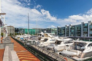 Ein Yachthafen mit mehreren festgemachten Yachten, einem Fußweg und modernen Gebäuden im Hintergrund.
