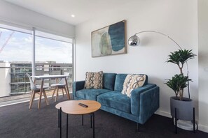 Una sala de estar moderna con un sofá azul, una mesa de centro redonda, una lámpara de pie y una planta en maceta.