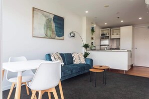 Ein modernes Wohnzimmer mit einer Couch, Sesseln, einem kleinen Tisch und einer Küchenzeile im Hintergrund.