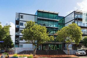 Un edificio moderno con fachada de vidrio, varios pisos y una escalera que lleva a la entrada.