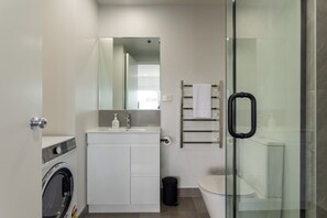 Un baño moderno con cabina de ducha de vidrio, lavadora integrada y un inodoro.
