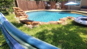 Un patio trasero con piscina, tobogán y una formación rocosa.