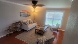 Una sala de estar con un sofá blanco, sillones estampados, una mesa de centro, una lámpara de pie y una estantería.