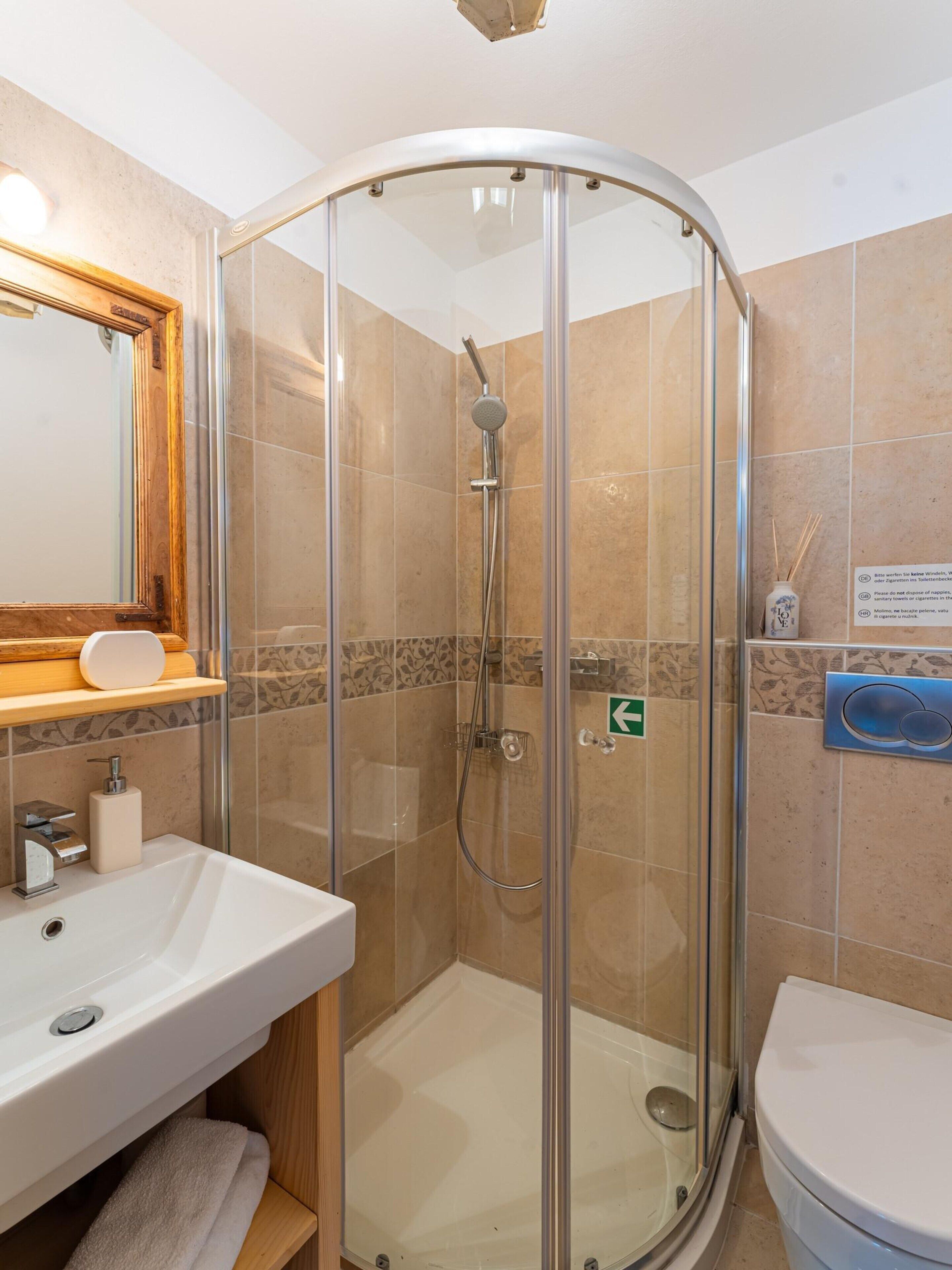 Un baño moderno con ducha acristalada, lavamanos con espejo e inodoro.
