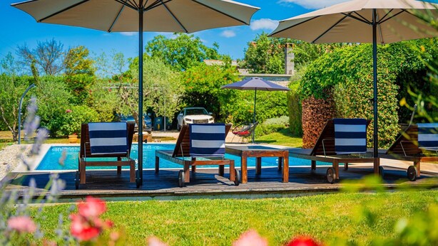 A poolside area with lounge chairs and umbrellas, surrounded by greenery and a clear sky. - Villa Benka With View (Tinjan)