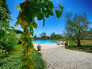 En swimmingpool omgivet af en grussti, med en terrasse og udendørs møbler.