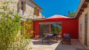 A patio with two lounge chairs and a red umbrella, a stone building with wooden shutters, and a potted plant. - Villa Benka With View (Tinjan)