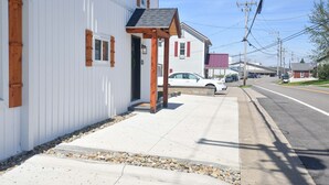 Un bâtiment blanc avec un porche en bois et une voiture garée devant.