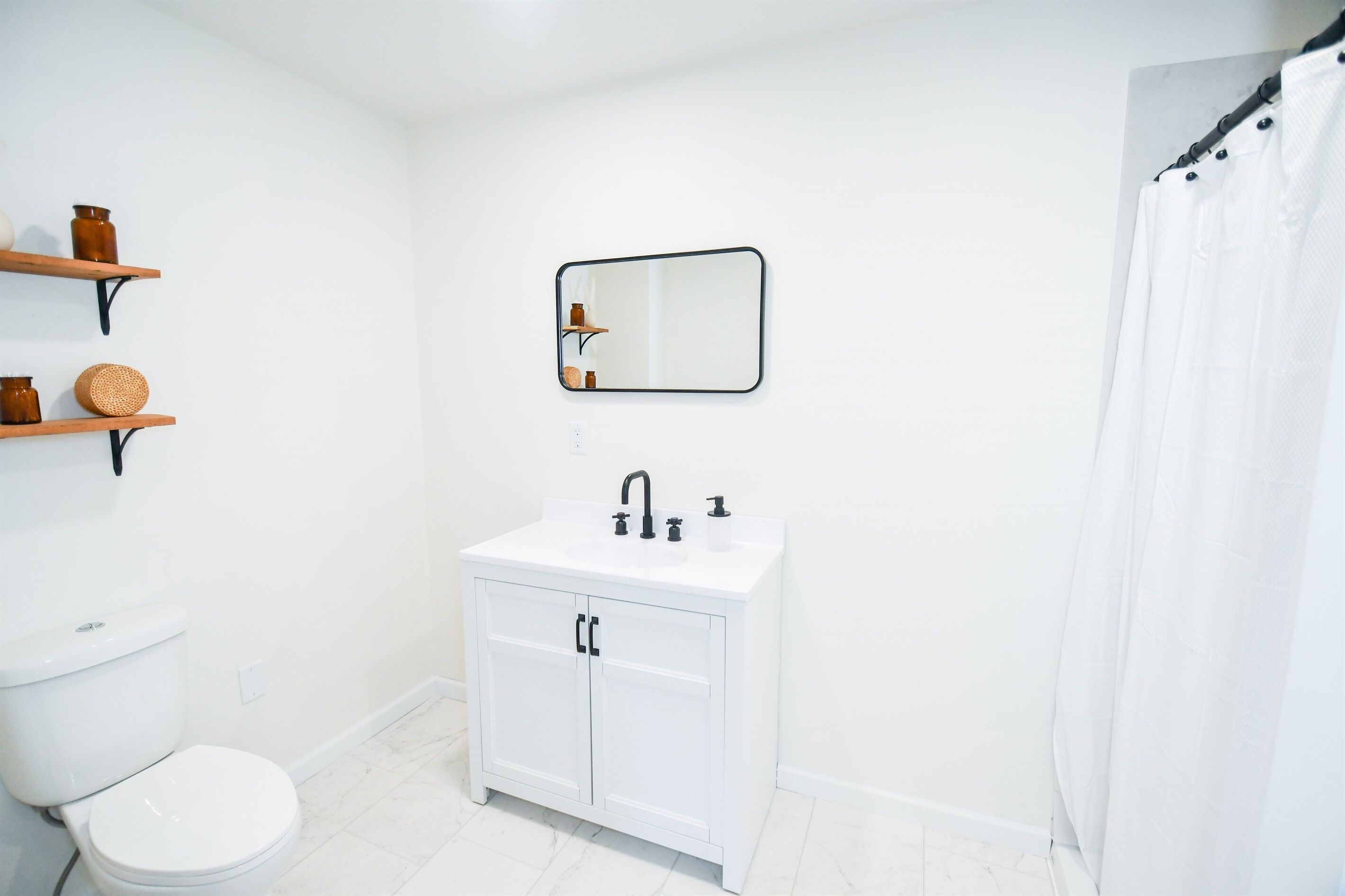 Ein Badezimmer mit Toilette, Waschbecken mit schwarzen Armaturen, einem Spiegel und einer Duschvorhang.