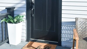 A black door with a green wreath, a doormat with "hello" written on it, and a wicker chair outside. - Boho Studio Downtown Amish Country + Scenic Views (Walnut Creek)