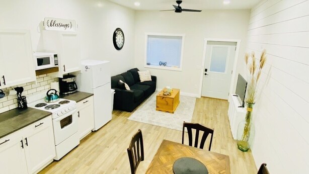 A compact kitchen with white cabinets, a microwave, stove, and a small dining area with a wooden table and chairs. - Anniversary Suite with a stunning country setting! (Sugarcreek)