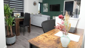 Ett modernt vardagsrum med ett matbord i trä, en grå soffa och en bärbar dator på ett skrivbord.
