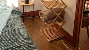A bedroom with a bed, a bedside table with a lamp, a wooden shelf with folded towels, and a window with curtains. - 3 rooms flat with garden next to the train station (Nevers)