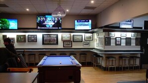 A billiards room with a pool table, bar area with stools, and multiple televisions displaying sports events. - The Caledonian Hotel (Wonthaggi)