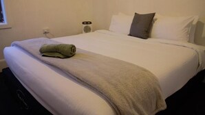 A neatly made bed with a green towel, white pillows, and a white blanket. - The Caledonian Hotel (Wonthaggi)