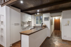A kitchen with white cabinets, a wooden countertop, a tiled backsplash, a window, and a door leading to another room.