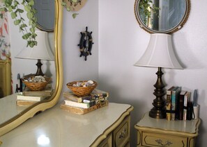 Une pièce comprenant un miroir, une lampe, une commode et une étagère murale où sont posés des livres et des objets décoratifs.