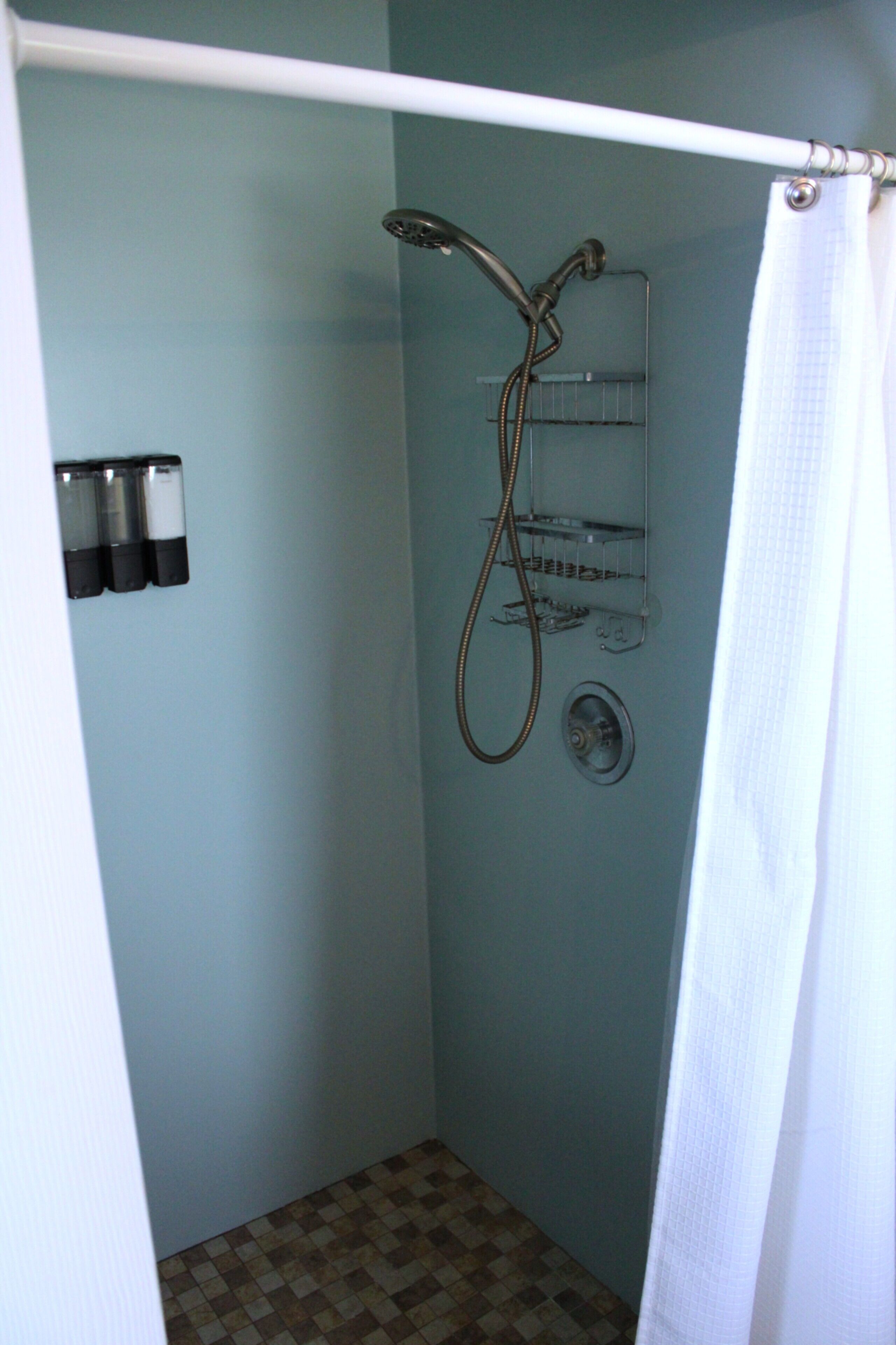 Un petit espace de douche fermé, comprenant un pommeau de douche, un porte-serviettes et un rideau de douche.