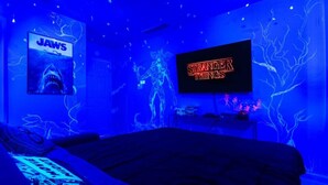 Une chambre avec un lit, un téléviseur diffusant la série « Stranger Things » et une affiche du film « Les Dents de la mer ».