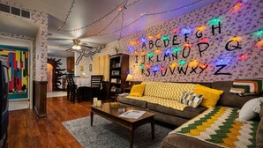 Un salon chaleureux avec un canapé en cuir marron, une table basse en bois et un tapis à motifs. Un mur est décoré d’un panneau lumineux représentant l’alphabet.