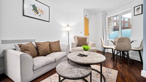Ein modernes Wohnzimmer mit einem grauen Sofa, einem runden Couchtisch und einem Essbereich mit Stühlen.