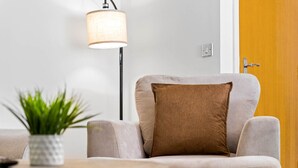 Ein modernes Wohnzimmer mit einer Couch, einem runden Tisch, einer Stehlampe und einer Topfpflanze.