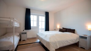 A bedroom with a bunk bed, a single bed, a window with curtains, bedside lamps, and a radiator. - Apartment in Bad Gastein Near Ski Lifts (Bad Gastein)