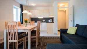 A modern kitchen with white cabinets, a dining table with chairs, and a dark-colored sofa. - Apartment in Bad Gastein Near Ski Lifts (Bad Gastein)