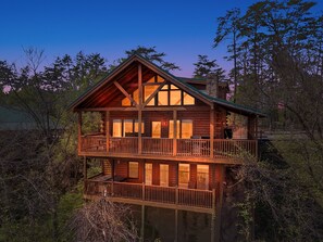 A two-story log cabin with a balcony, surrounded by trees. - Theater Room 🎬 85” TV | Hot Tub | Pool Table | Mountain Views | Near Parkway | Sleeps 12 (Pigeon Forge)