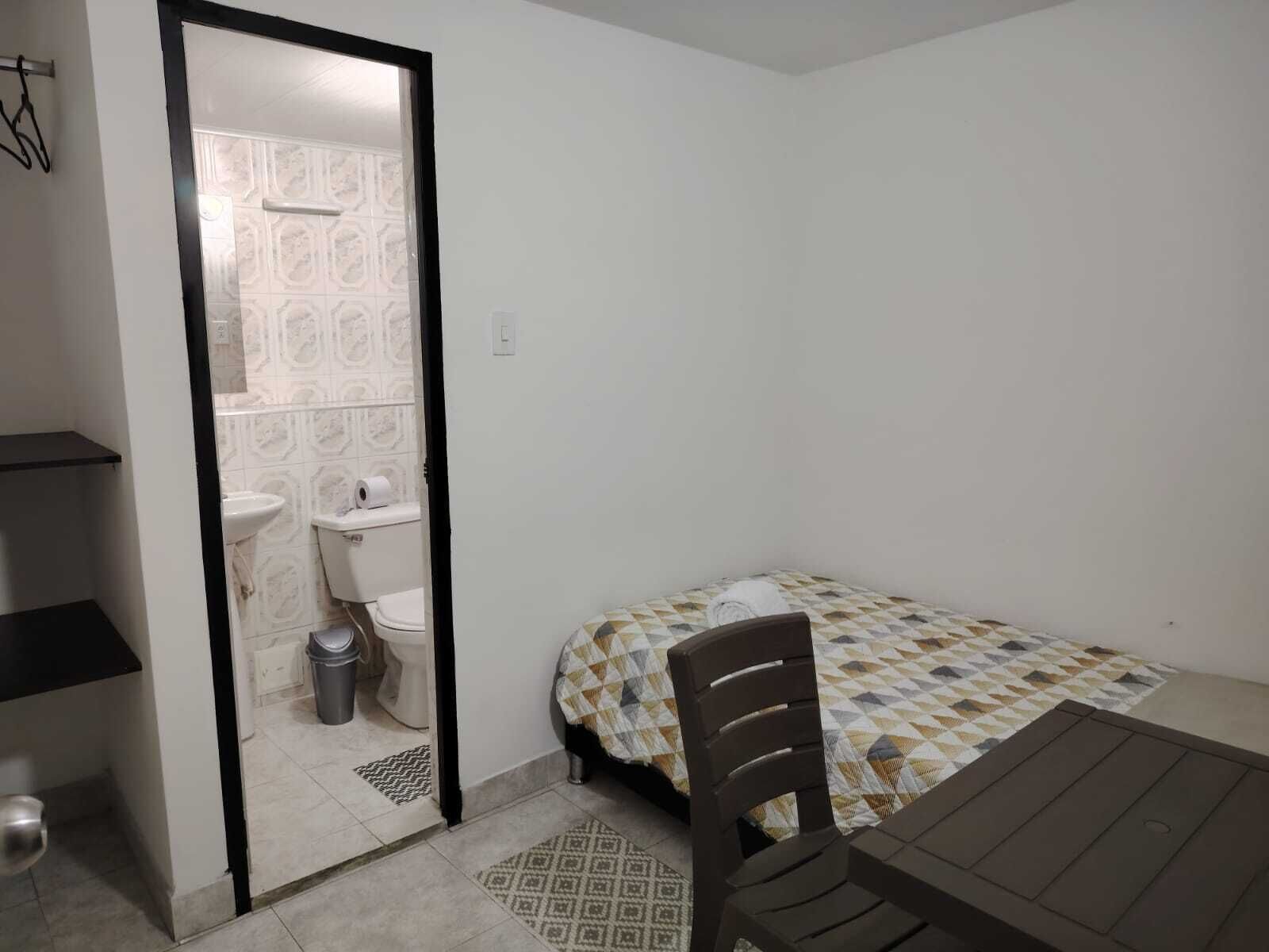 A small, clean room with a bed, a table, and a bathroom visible through an open door.
