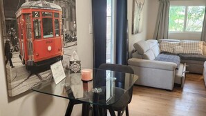 A cozy living room with a sofa, a glass coffee table, and a red vintage tram displayed on the wall. - Charming studio in delightful Spring Branch for a quick, tranquil stay.   (Spring Branch)