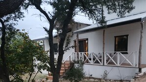 A white building with a wooden porch and a stone pathway leading to it. - Charming studio in delightful Spring Branch for a quick, tranquil stay.   (Spring Branch)
