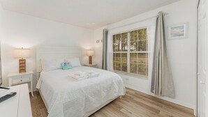 Une chambre à coucher avec un grand lit, deux tables de chevet avec des lampes, une fenêtre avec des stores et une porte.