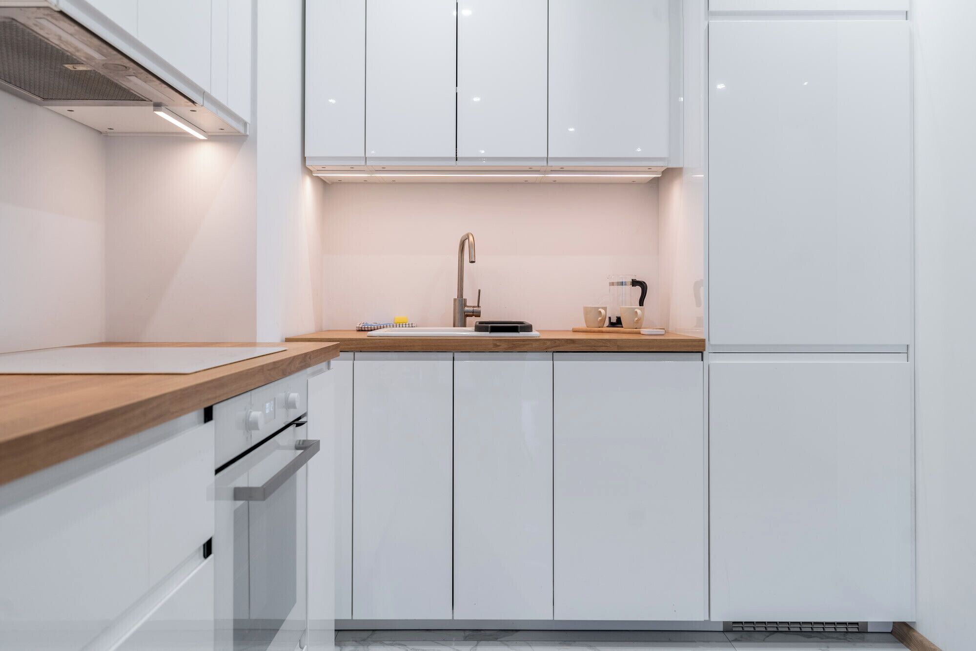 Una cocina moderna con armarios blancos, encimera de madera, pileta de acero inoxidable y horno empotrado.