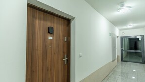 A hallway with a wooden door marked with the number 16, a glass elevator door, and a tiled floor. - Park Śląski Homely Apartment #16 (Katowice)