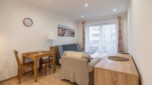 A small, cozy room with a wooden dining table, a sofa, and a window with a view of buildings. - Park Śląski Homely Apartment #16 (Katowice)