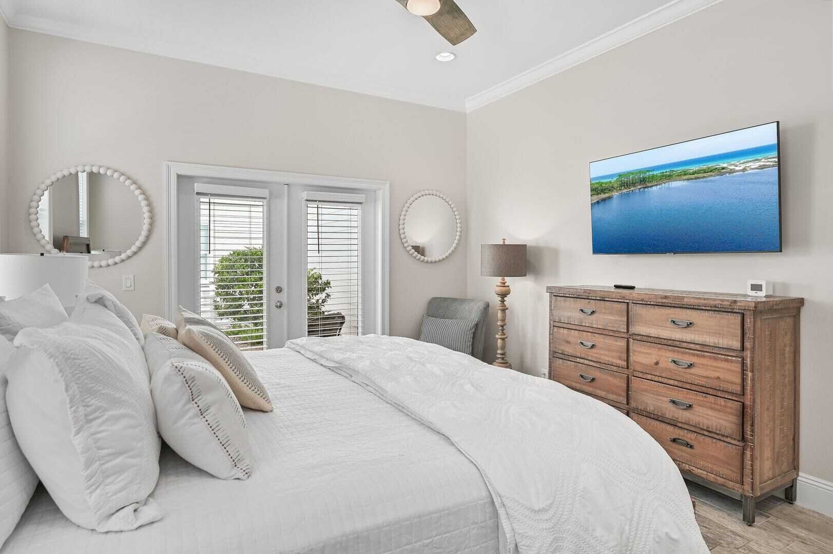 Une chambre à coucher avec un grand lit, une commode, un miroir et un téléviseur fixé au mur.