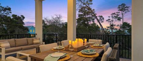 A covered outdoor patio with a wooden table set for dining, surrounded by cushioned seating.