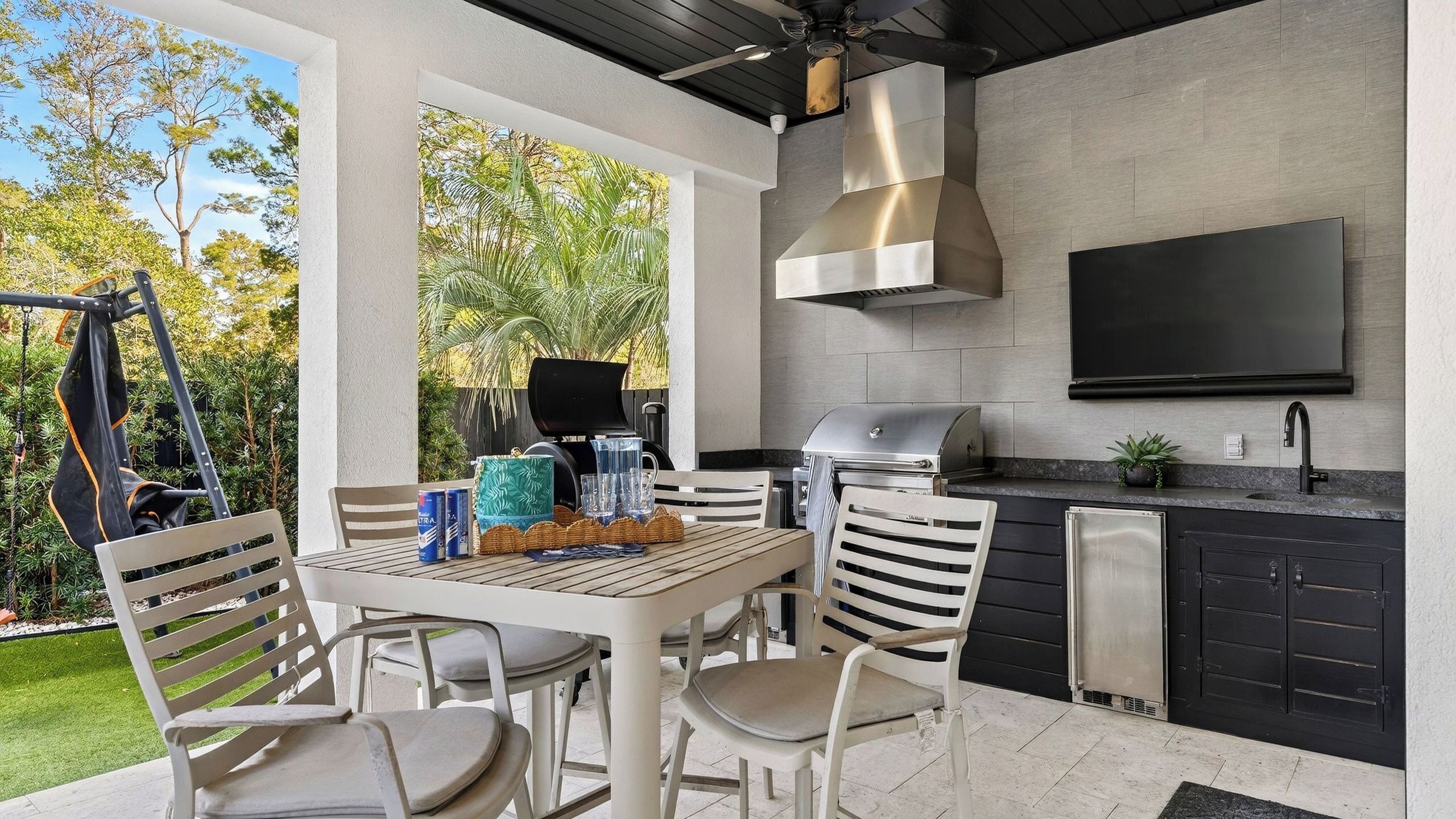 An outdoor kitchen with a grill, a TV, and a dining area with chairs and a table.