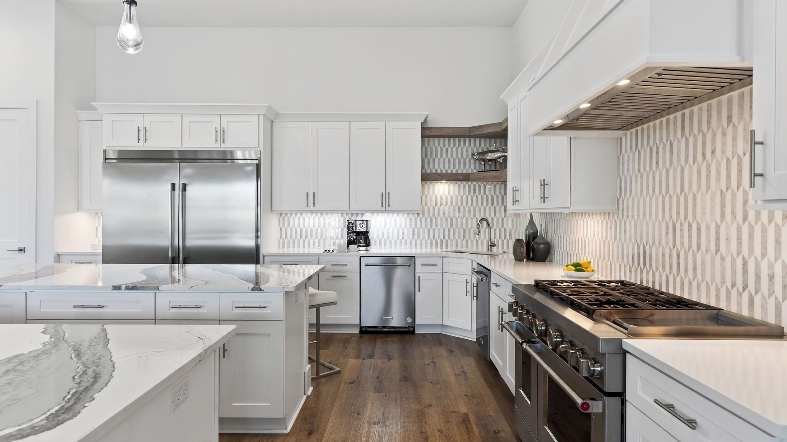 A modern kitchen with white cabinetry, stainless steel appliances, a marble countertop, and a patterned backsplash.