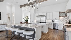 Una cocina moderna con una isla central, taburetes de bar, electrodomésticos de acero inoxidable e iluminación colgante.