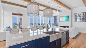 Une cuisine moderne dotée d’un grand îlot central, de meubles bleus et offrant une vue sur l’océan.