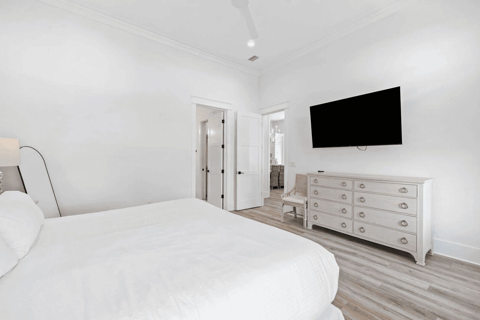 A bedroom with a large bed, a dresser, a television mounted on the wall, and a door leading to another room.