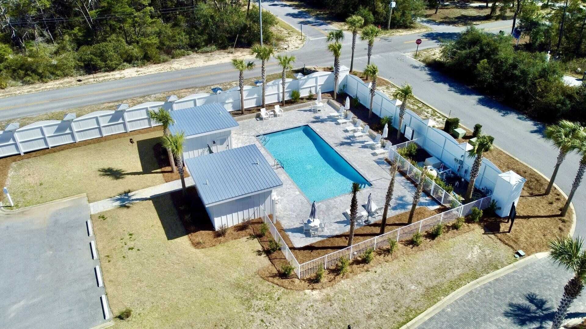 An aerial view of a property with a swimming pool, white fences, and palm trees.