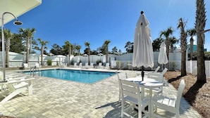 A swimming pool with white lounge chairs and umbrellas, surrounded by palm trees and a clear blue sky.