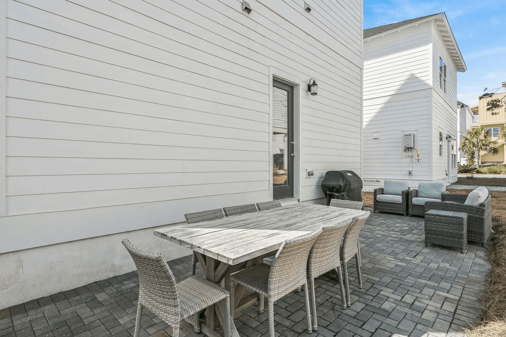 A patio with a wooden table and wicker chairs, a grill, and a covered seating area.