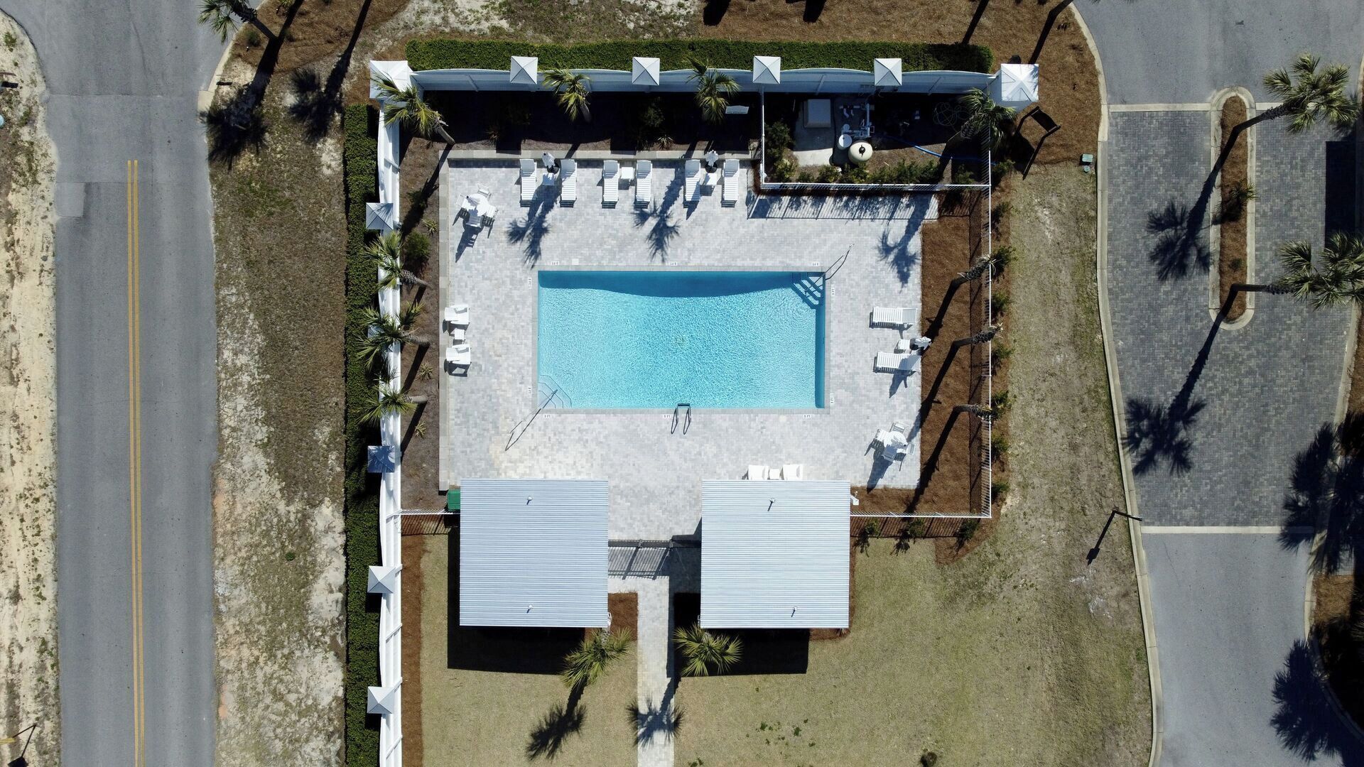 Vista aérea de un área de piscina con sillones de descanso, una alberca y un porche cubierto.